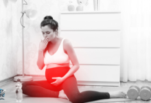 امرأة حامل تجلس على الأرض وتغطي فمها بيدها، تبدو متأثرة برائحة كريهة.