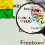 خريطة تُظهر موقع دولة غينيا بيساو في غرب إفريقيا تحت عدسة مكبرة، مع ظهور علم الدولة في الزاوية.