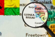 خريطة تُظهر موقع دولة غينيا بيساو في غرب إفريقيا تحت عدسة مكبرة، مع ظهور علم الدولة في الزاوية.