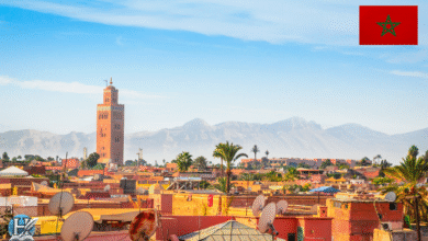 منظر لمدينة مراكش المغربية يظهر فيه جامع الكتبية وخلفه جبال الأطلس تحت سماء صافية.