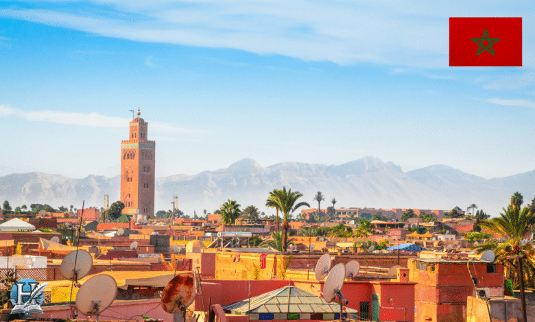 منظر لمدينة مراكش المغربية يظهر فيه جامع الكتبية وخلفه جبال الأطلس تحت سماء صافية.