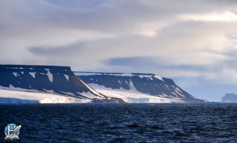 مشهد طبيعي من سواحل المحيط المتجمد الشمالي يظهر فيه الجليد والجبال المغطاة بالثلوج تحت سماء غائمة.