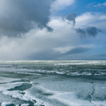 مشهد واسع للمحيط الجنوبي المتجمد، تُغطيه طبقات من الجليد العائم تحت سماء غائمة وزرقاء.