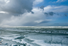 مشهد واسع للمحيط الجنوبي المتجمد، تُغطيه طبقات من الجليد العائم تحت سماء غائمة وزرقاء.