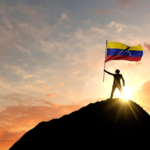 شخص يقف على قمة جبل رافعاً علم فنزويلا عند غروب الشمس، يرمز لقوة الدولة وتحدياتها السياسية المعاصرة.