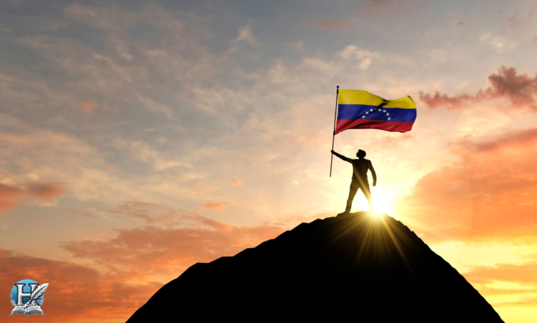 شخص يقف على قمة جبل رافعاً علم فنزويلا عند غروب الشمس، يرمز لقوة الدولة وتحدياتها السياسية المعاصرة.